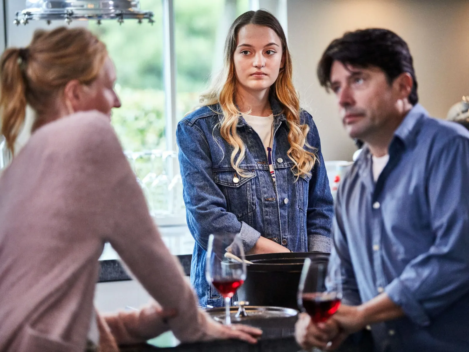Een tienermeisje kijkt bedenkelijk naar haar vader en zijn nieuwe partner in de keuken