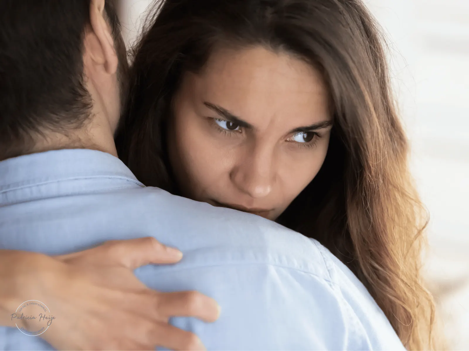 Een vrouw kijkt twijfelend over de schouder van haar partner terwijl ze hem omhelst